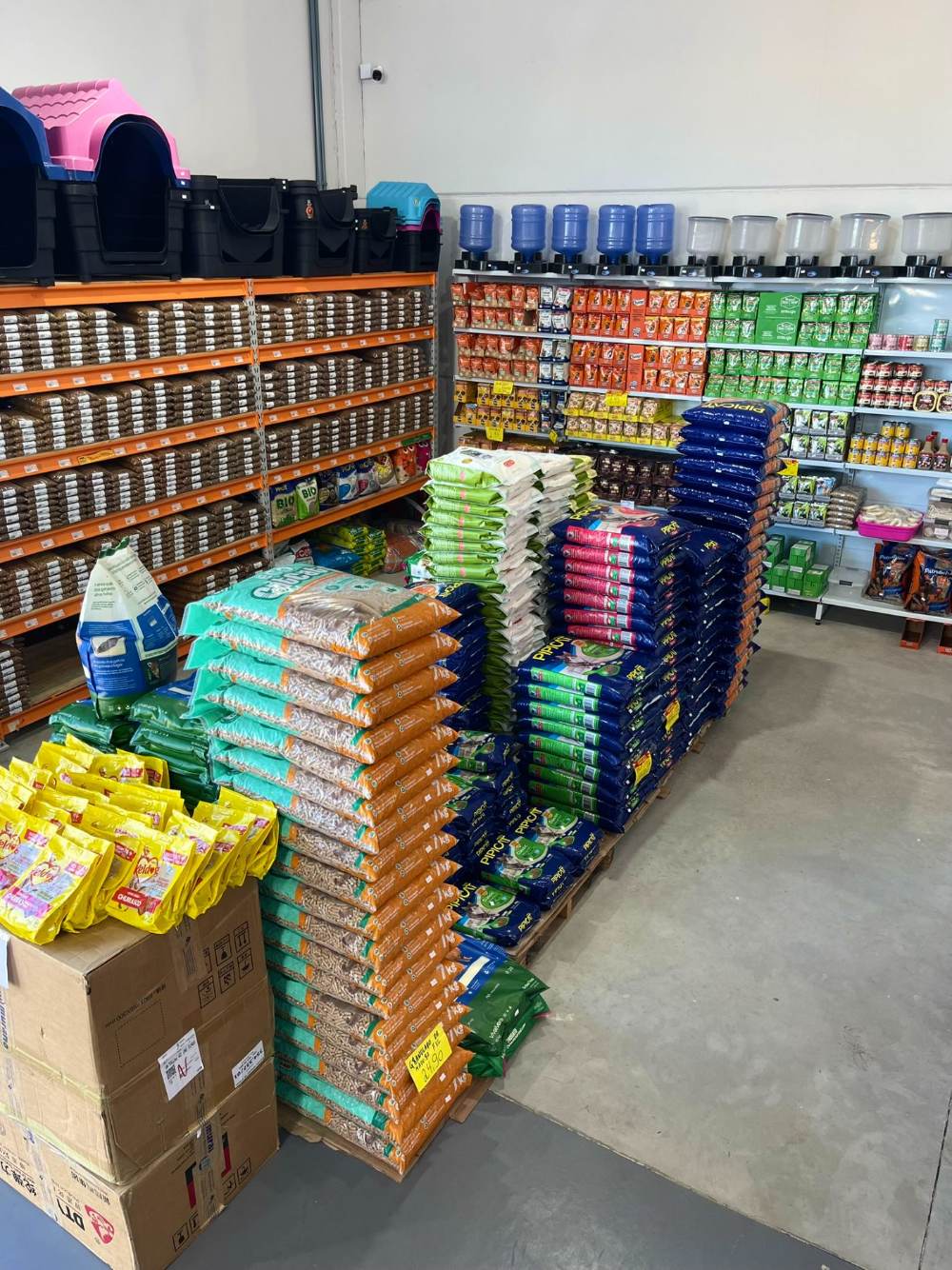 Pilhas de granulado e maravalha ao lado de prateleiras de areia higiênica e alimentos úmidos.